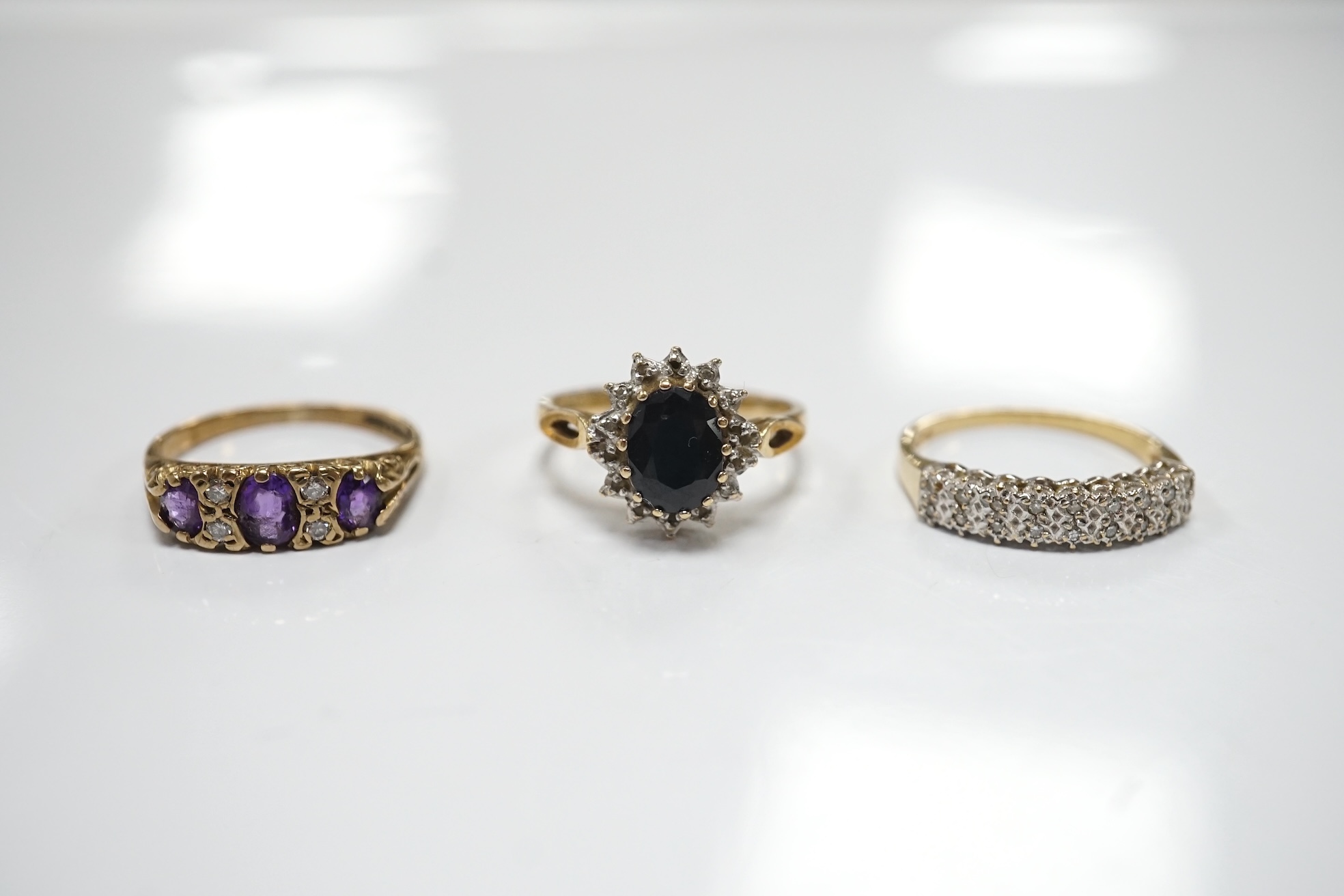 Three assorted 9ct and gem set rings including a diamond chip cluster half hoop and two pairs of yellow metal and gem set ear studs including sapphire? and diamond cluster. Condition - fair to good